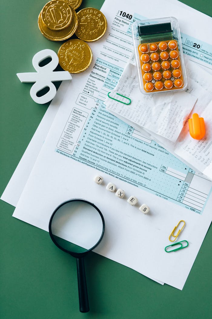 hero-img-02 Top view of tax forms, calculator, coins, and office supplies on a green desk.